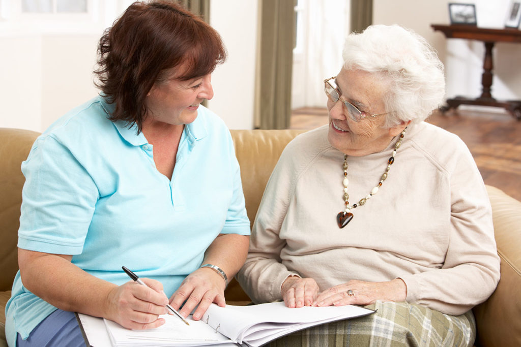 Photo-3_GetStarted an image of a middle-aged woman helping her elderly mother fill out paper work as they both sit together on a couch inside a brightly lit room